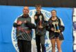 Three athletes are photographed during a kickboxing tournament posing in front of a blue banner.
