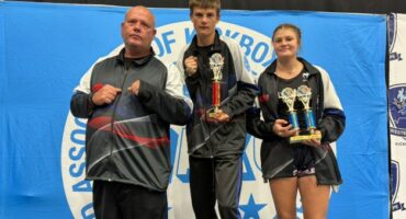 Three athletes are photographed during a kickboxing tournament posing in front of a blue banner.