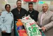 Four people are photographed in a supermarket with a trolley filled with a food donation.