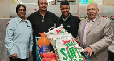 Four people are photographed in a supermarket with a trolley filled with a food donation.