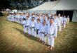 A photo taken of a large group of people dressed in karate attire standing outside a big white tent.