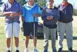 Four men photographed in their golfing attire on a golf coarse.