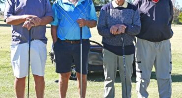 Four men photographed in their golfing attire on a golf coarse.