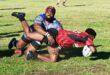 A photo taken of two rugby players tackling one another on the rugby field.