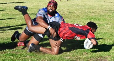 A photo taken of two rugby players tackling one another on the rugby field.