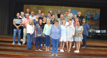 Group of former Dundee High students standing in a group on the stage in the school hall.