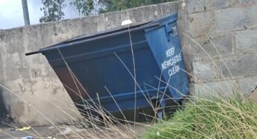 A blue municipal skip bin standing outside.