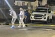 Image of men in protective gear adjacent to crime scene tape.