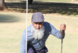 Image of golfer A Khan kneeling next to a hole on the Dundee golf course celebrating a hole-in -one.