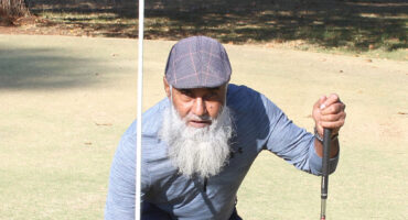 Image of golfer A Khan kneeling next to a hole on the Dundee golf course celebrating a hole-in -one.