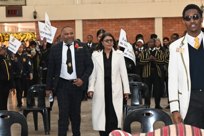 A celebration is photographed inside a school hall, wishing its school principal farewell.
