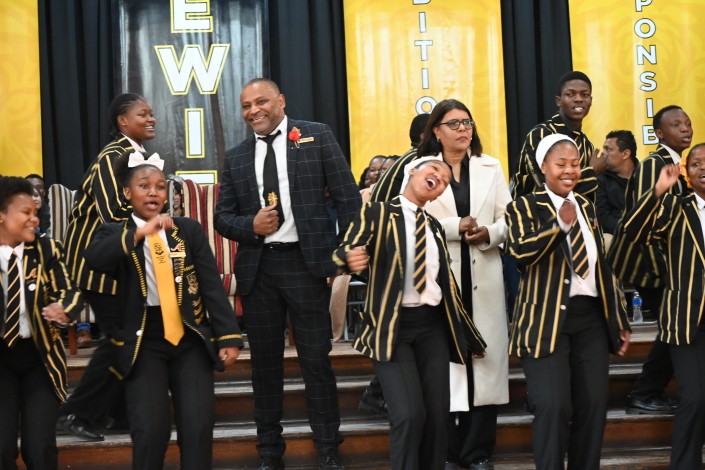 A celebration is photographed inside a school hall, wishing its school principal farewell.