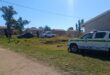A photo taken in a rural area of a police car outside a homestead. Two other vehicles are seen in the photo with several members of the public standing outside.