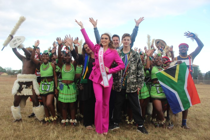 A girl dressed in pink and her family are photographed with a group of Zulu dancers in an open field.