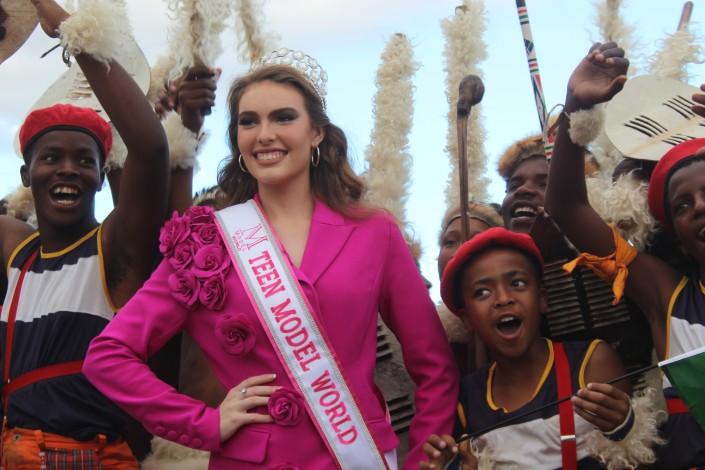 A girl dressed in pink and her family are photographed with a group of Zulu dancers in an open field.