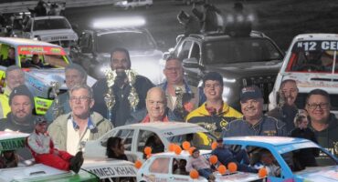 A black and white photo used a main background image of cars going around a race track. In the forefront is several colour photos of race cars as well as a group of people holding trophys.