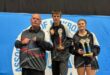 Three athletes are photographed during a kickboxing tournament posing in front of a blue banner.