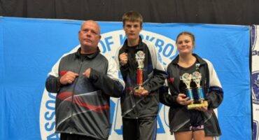 Three athletes are photographed during a kickboxing tournament posing in front of a blue banner.