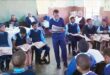 Image of learners reading from newspapers watched by educators and parents.