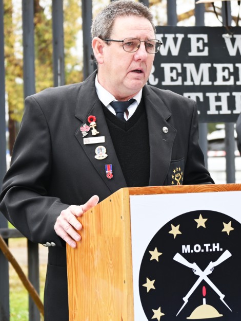 A man dressed in MOTH attire is photographed giving a formal speech outside the shellhole. 
