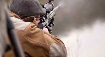 Image of a man in cap hodling a rifle and firing it.