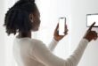 A woman wearing white attire and standing at a white wall is busy on her smart phone and her smart prepaid metre.