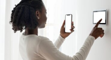 A woman wearing white attire and standing at a white wall is busy on her smart phone and her smart prepaid metre.