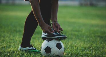 Soccer player posing with his foot on a soccer ball on a green field.