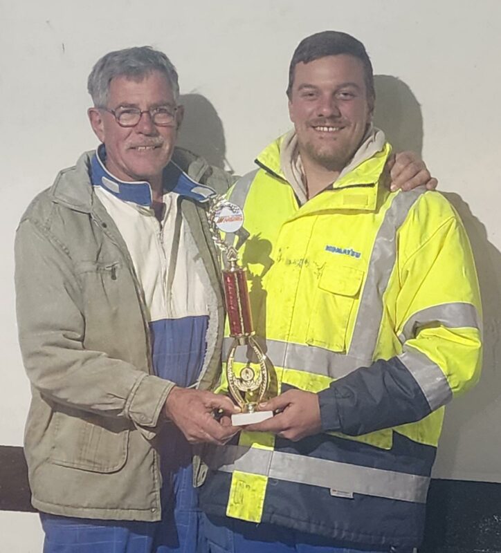 A photograph of a father and his son sharing a trophy.