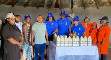 Image of Nontsikelelo Mhlongo, owner of Mhlongo Omhle, standing with Umzinyathi officials behind her dairy products.