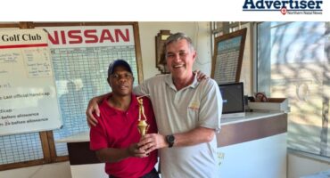 Two golfers photographed in a clubhouse holding a trophy.