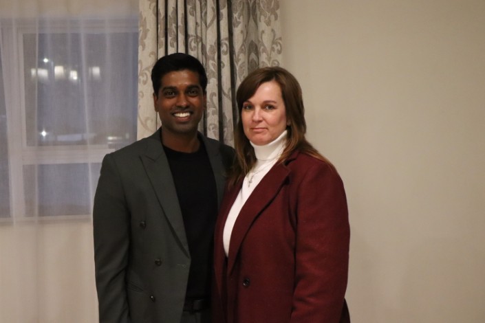 A photographed of a man wearing a black and grey suite standing next to a woman in a maroon and white suite.
