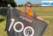 Image of a woman holding a 100th milestone parkrun flag.