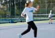 Image of a girl playing tennis with her back to the camera,