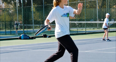 Image of a girl playing tennis with her back to the camera,