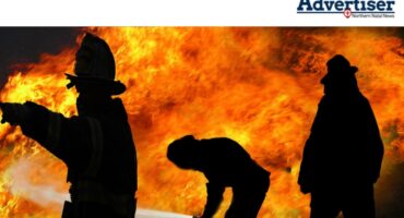 Three siluettes of fire fighters fighting a fire.