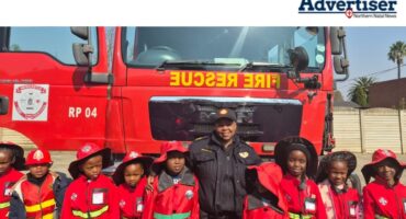 A photo of a group of school children posing with a fire fighter in front of a fire truck.