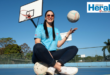 Image of woman with netball ball sitting on a netball court.