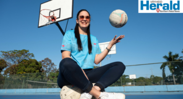 Image of woman with netball ball sitting on a netball court.