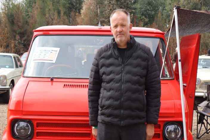 A man photographed standing in front of a red vintage combi.
