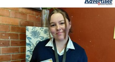A young girl is photographed holding a medal and certificates inside a school office.