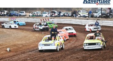Several oval track cars are photographed on a dirt track.