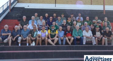 A large group of elderly, former Newcastle rugby players sitting on a pavillion.