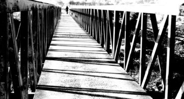 Black and white image of a foot bridge covered in frost in early morning sun.