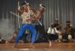 Image of two school learners dressed in traditional Zulu garb stick fighting.