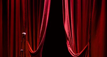 Image of red curtains parted on a stage.