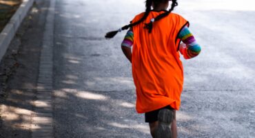 Image of a girl running on road with back to the camera.
