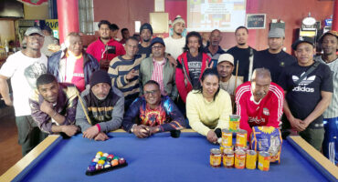 Image of pool players around a pool table with tins of pet food donated to the Dundee SPCA.