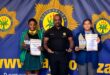 Image of uniformed school children in front of SAPS badge with a police spokespeson in Dundee area.