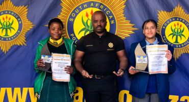 Image of uniformed school children in front of SAPS badge with a police spokespeson in Dundee area.